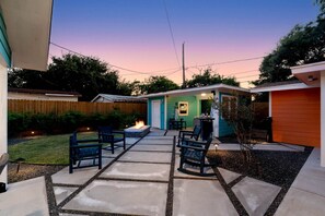 A backyard patio with a fire pit, outdoor seating, and a small building with a neon sign.