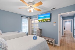 A bedroom with two beds, a ceiling fan, a painting of a beach, and a hallway leading to another room. - Newly Remodeled 3 Bed/2 Bath, Hot Tub, Pet Friendly, Corpus Christi (Corpus Christi)