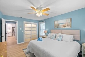 A bedroom with a bed, a ceiling fan, a door leading to a bathroom, and a painting on the wall. - Newly Remodeled 3 Bed/2 Bath, Hot Tub, Pet Friendly, Corpus Christi (Corpus Christi)