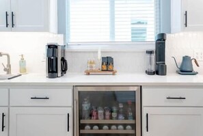 A kitchen with white cabinets, a coffee maker, a kettle, and a window with blinds.