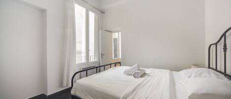 A bedroom with a bed, a window with curtains, and a radiator.