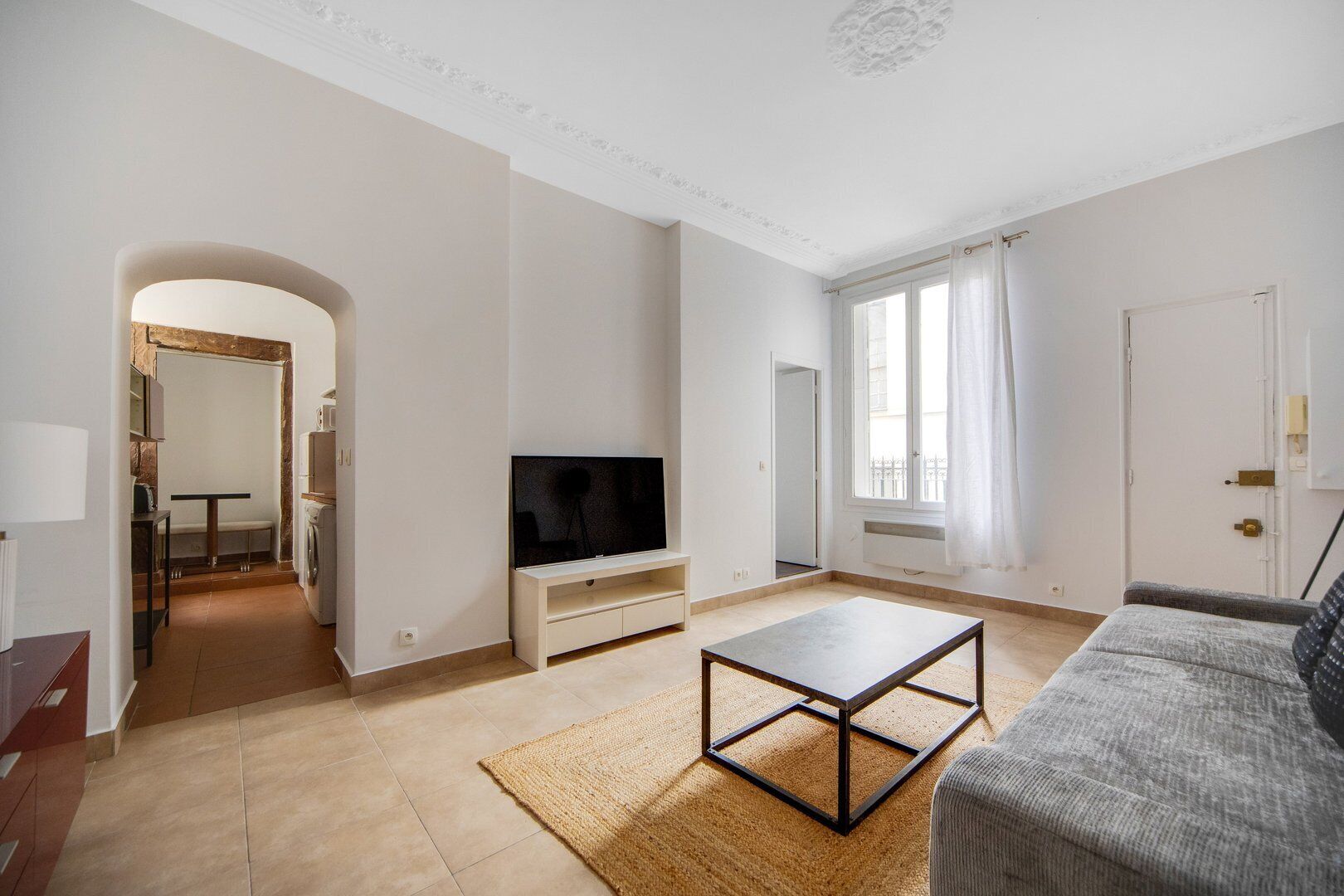Un salon spacieux équipé d’un téléviseur à écran plat, d’une table basse et d’un canapé. Il y a également un coin buanderie avec un lave-linge et une table. La pièce est dotée de grandes fenêtres avec des rideaux et d’une porte qui donne sur une autre pièce.
