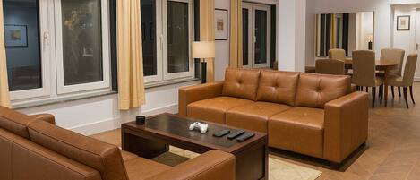 A modern living room with a brown leather sofa, a coffee table, and a dining area in the background.