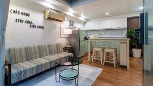 A compact living space with a sofa, a small round table, a kitchenette, and a glass partition.