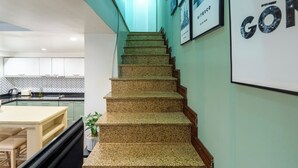 A staircase leading to a kitchen area with a herringbone-patterned backsplash, a dining table, and chairs.