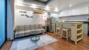 A compact living space with a sofa, a small round table, a kitchen area with a fridge, and a herringbone-patterned backsplash.