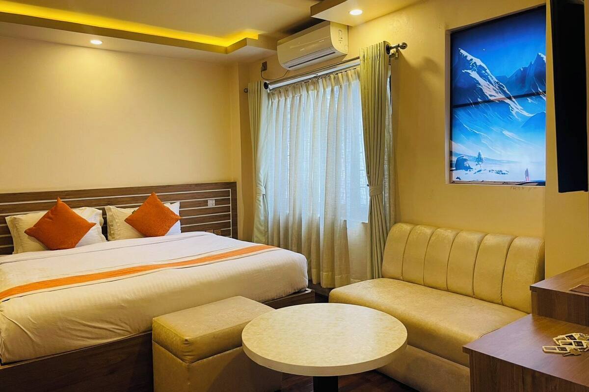 A hotel room with a bed, a sofa, a small round table, and a large window with curtains.