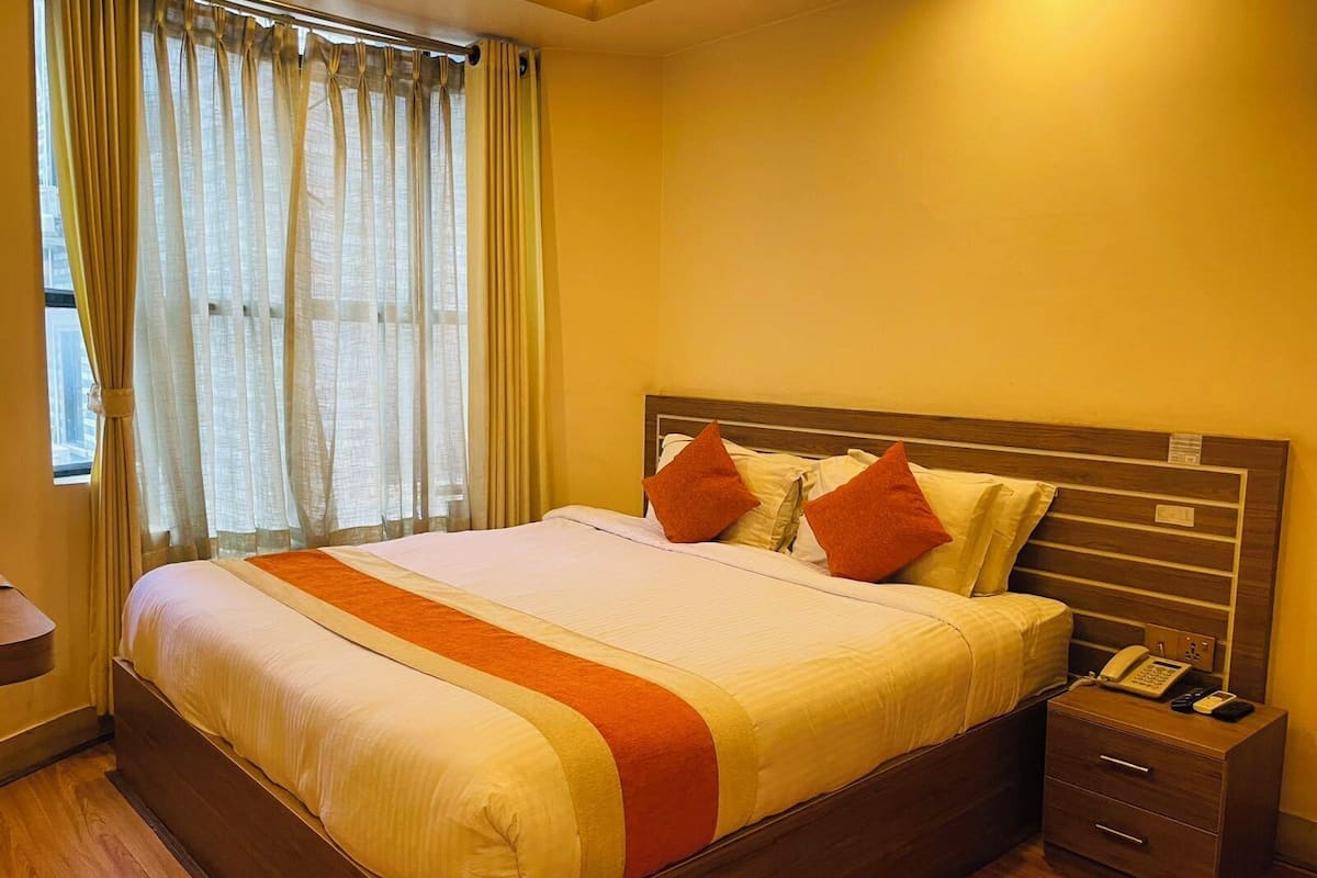 A hotel room with a large bed, wooden headboard, and a bedside table with a phone.