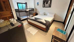 Une chambre d’hôtel avec des lits superposés, un bureau avec un ordinateur, une table de chevet et une fenêtre avec des rideaux.
