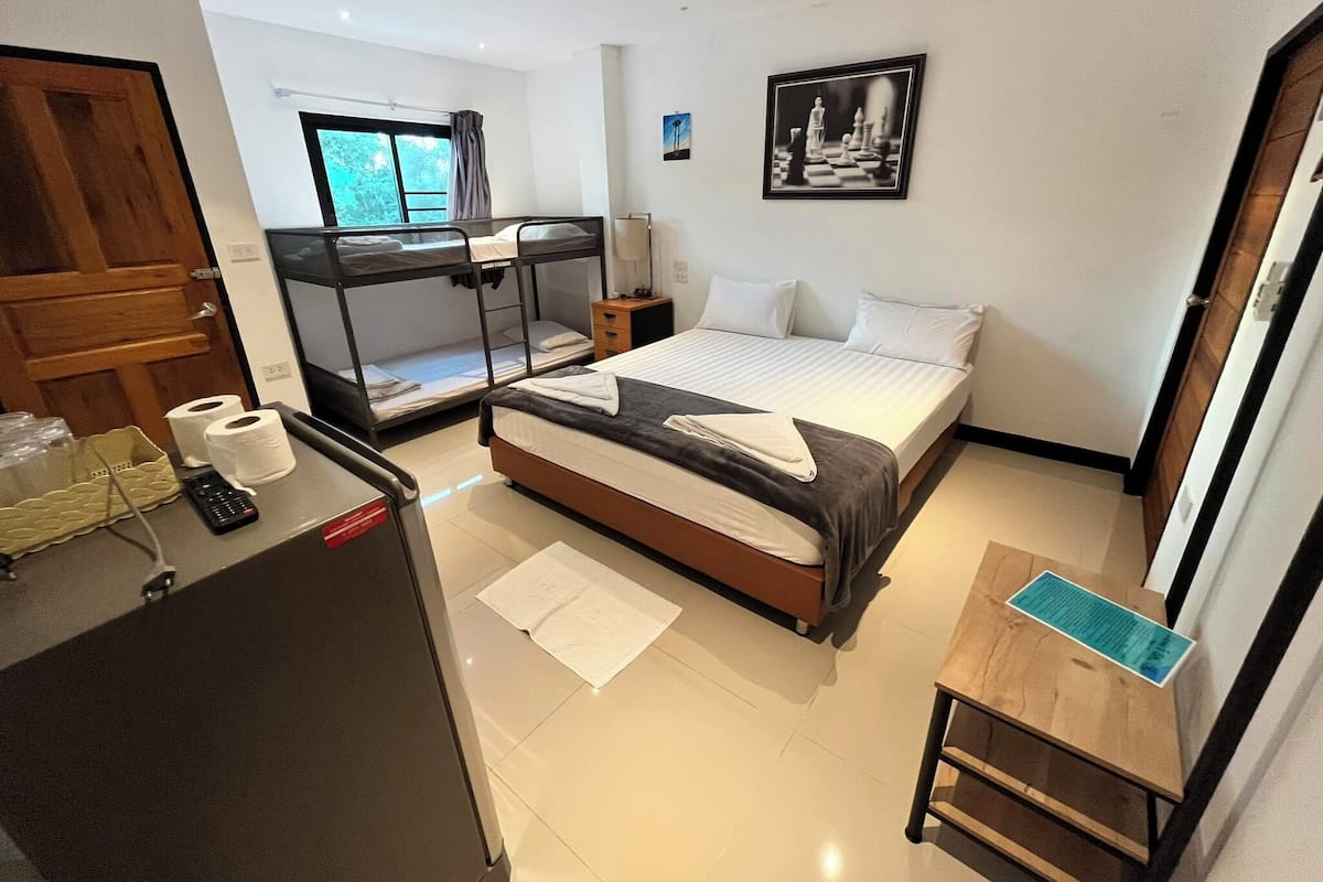 A hotel room with bunk beds, a desk with a computer, a bedside table, and a window with curtains.