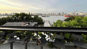 Vue sur les gratte-ciel d’une ville, prise depuis un balcon, avec une rivière et des bateaux au premier plan.