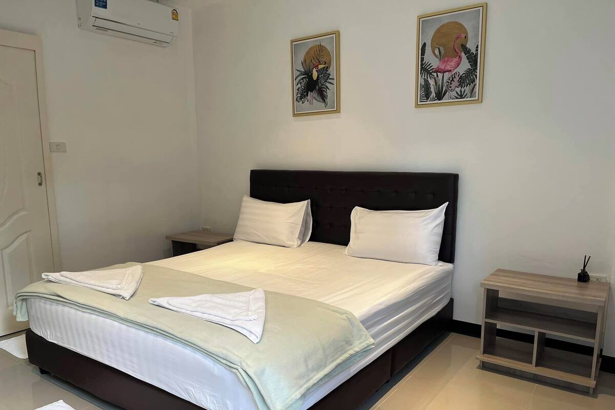 A neatly made bed with white linens, a dark headboard, and two wall-mounted paintings of birds.