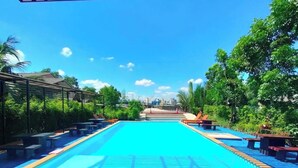 Une piscine à l’eau d’un bleu cristallin, entourée de chaises longues et de zones ombragées, avec une vue sur la ville en arrière-plan.