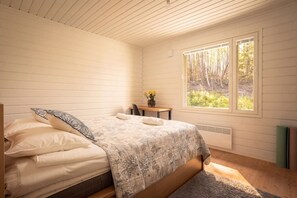 Ein Schlafzimmer mit einem Bett, einem kleinen Tisch mit Blumen und einem Fenster mit Blick auf einen Wald.