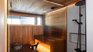 A sauna room with wooden benches, a sauna heater, and a shower area. - Stay North - Parmaranta (Ylöjärvi)