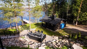 A lakeside cabin with outdoor seating, a deck, and a small structure with a blue sign. - Stay North - Parmaranta (Ylöjärvi)