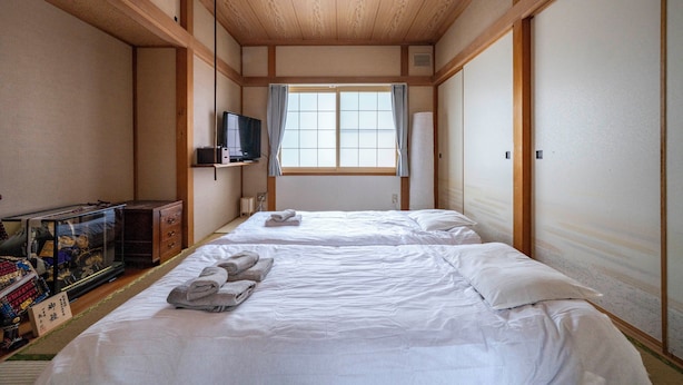 A traditional Japanese-style room with two beds, a television, and a sliding door. - KOTONOHA (Otaru)