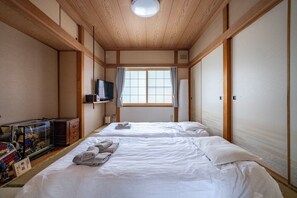 A traditional Japanese-style room with two beds, a television, and a sliding door. - KOTONOHA (Otaru)