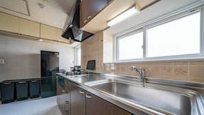 A modern kitchen with a stainless steel sink, wooden cabinets, and a window providing natural light. - KOTONOHA (Otaru)