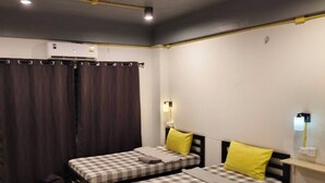 Une chambre avec deux lits, chacun recouvert d’une courtepointe à carreaux et doté d’un oreiller, un plancher en bois, un plafond avec des poutres apparentes et un appareil de climatisation.
