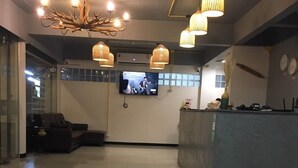 Un hall d’entrée moderne doté d’un comptoir de réception, d’un espace salon confortable et d’un grand téléviseur à écran plat fixé au mur.