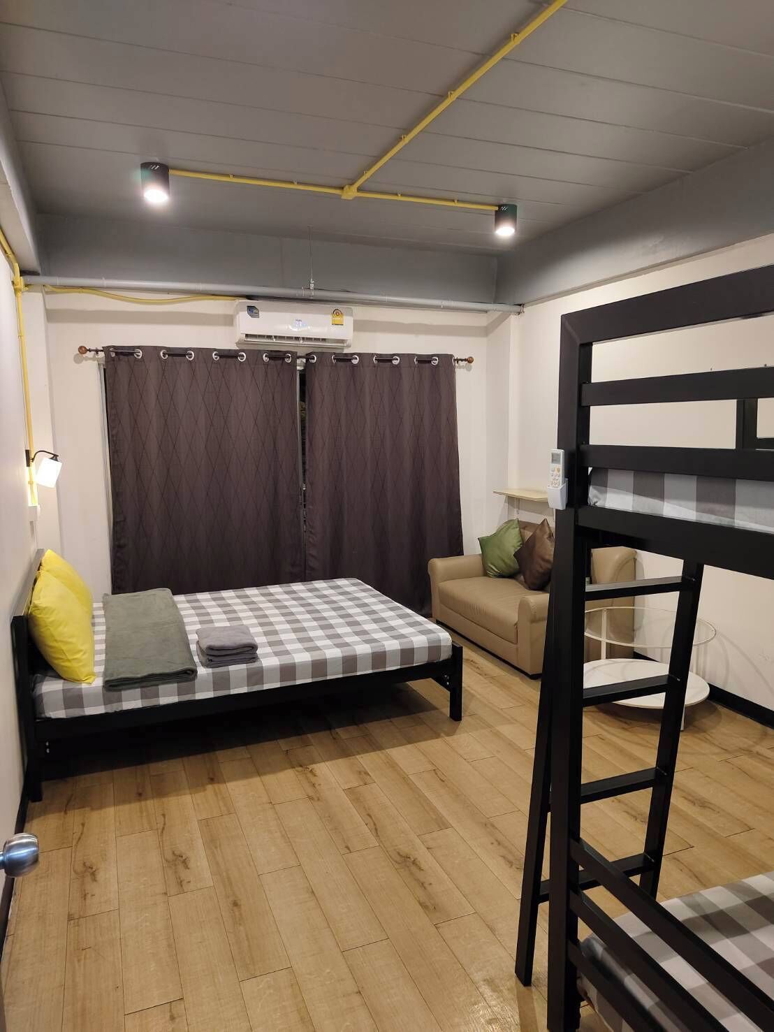A compact room with a bed, a sofa, a bunk bed, and an air conditioning unit.