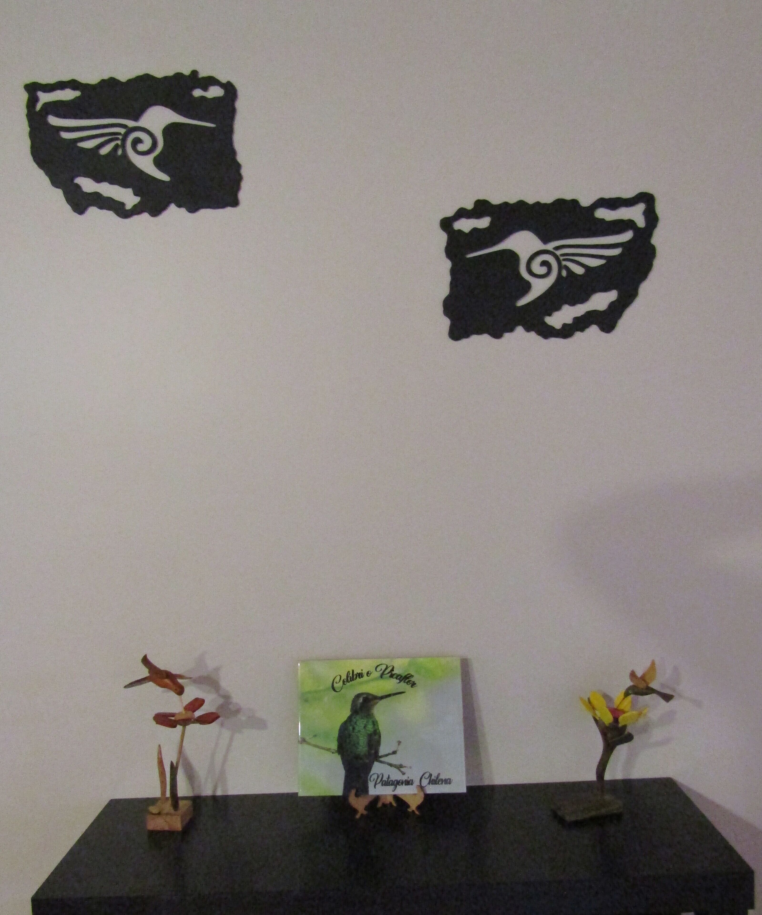 A wall with two black decorative cutouts and a central display with a book and two small plant arrangements.