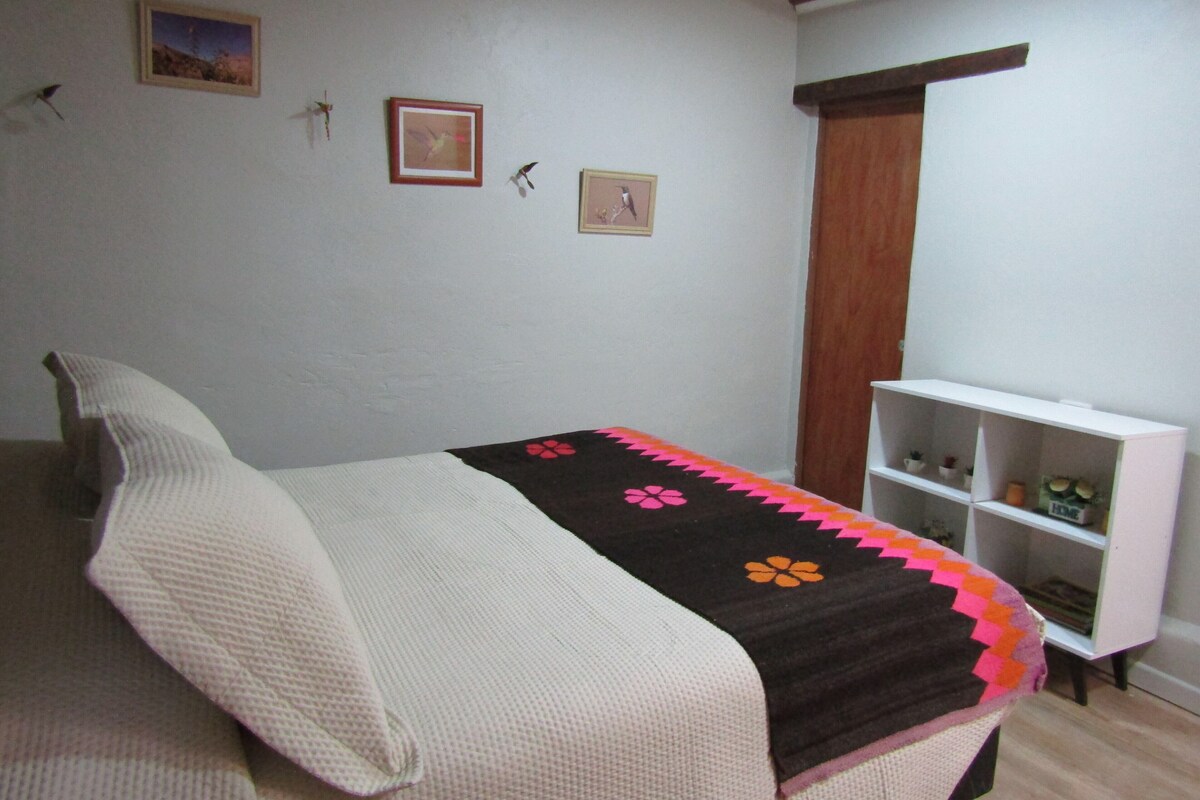 Un dormitorio con una cama, un estante blanco con objetos decorativos y dos cuadros en la pared.