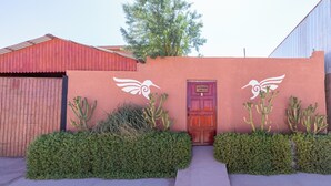 Une façade d’immeuble avec une porte rouge, deux fresques représentant des oiseaux blancs et des cactus.