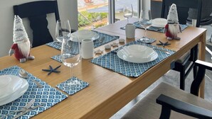 Un coin repas avec vue sur la plage, une table en bois dressée avec des assiettes, des verres et des étoiles de mer, ainsi que deux décorations représentant des gnomes.