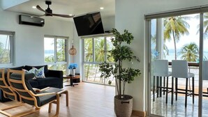Un vaste espace de vie agrémenté d’une grande fenêtre, d’un ventilateur de plafond, d’un téléviseur à écran plat et d’une plante en pot.