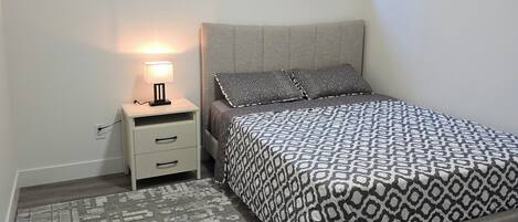 Un dormitorio con cama, mesita de noche, lámpara y ventana con persianas.