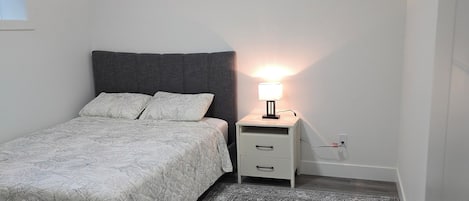 Et soveværelse med seng, sengebord, lampe og tæppe.