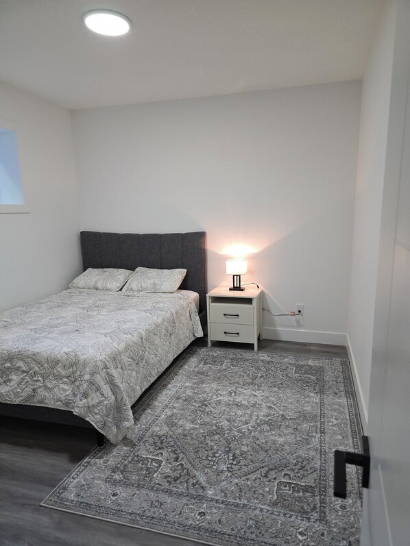 A bedroom with a bed, bedside table, lamp, and rug.