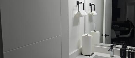 Et badeværelse med en hvid vask, to sorte håndklædeholdere, et spejl og en toiletpapirholder.