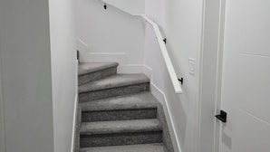 A staircase with carpeted steps, white walls, and a white door.