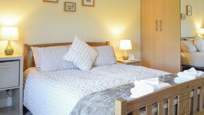 A neatly made bed with a wooden headboard, two bedside tables with lamps, a wardrobe, and framed pictures on the wall.