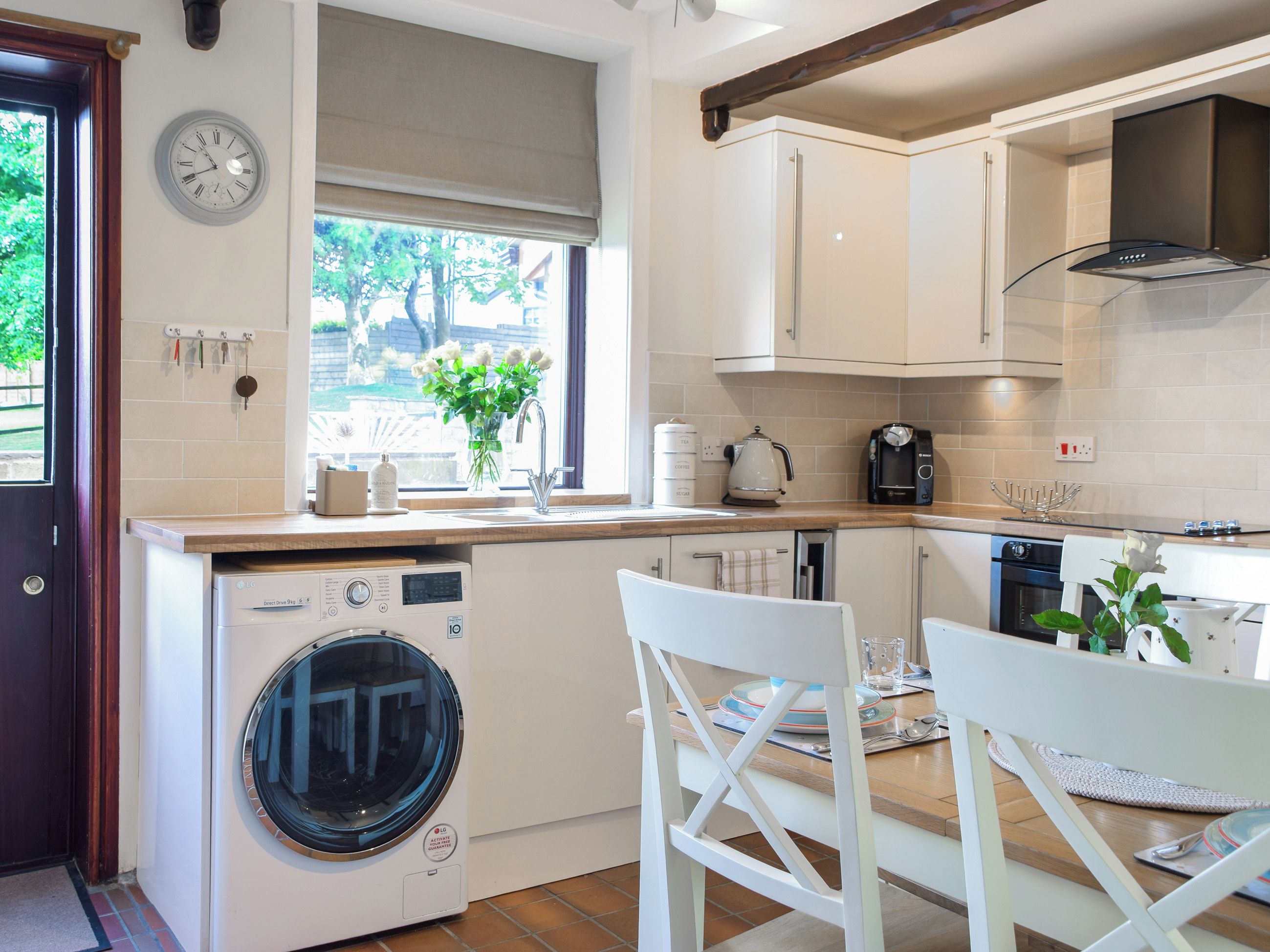 A kitchen with a washing machine, a dining area with chairs, and a window with a view of trees.