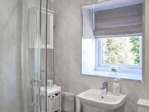 Une salle de bain avec une douche à parois de verre, un lavabo placé sous une fenêtre et un porte-serviettes.