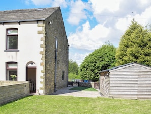 Un bâtiment en pierre avec un toit en pente, un petit abri en bois et une cour couverte d’herbe.