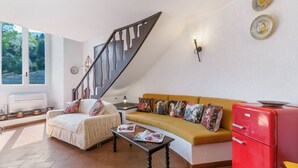 A living room with a sofa, a coffee table, a red cabinet, a staircase, and a window with a view of trees. - Albert's Castle Apt (Baveno)