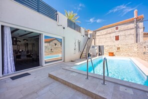 A modern villa with a swimming pool, a dining area, and a view of the surrounding buildings.