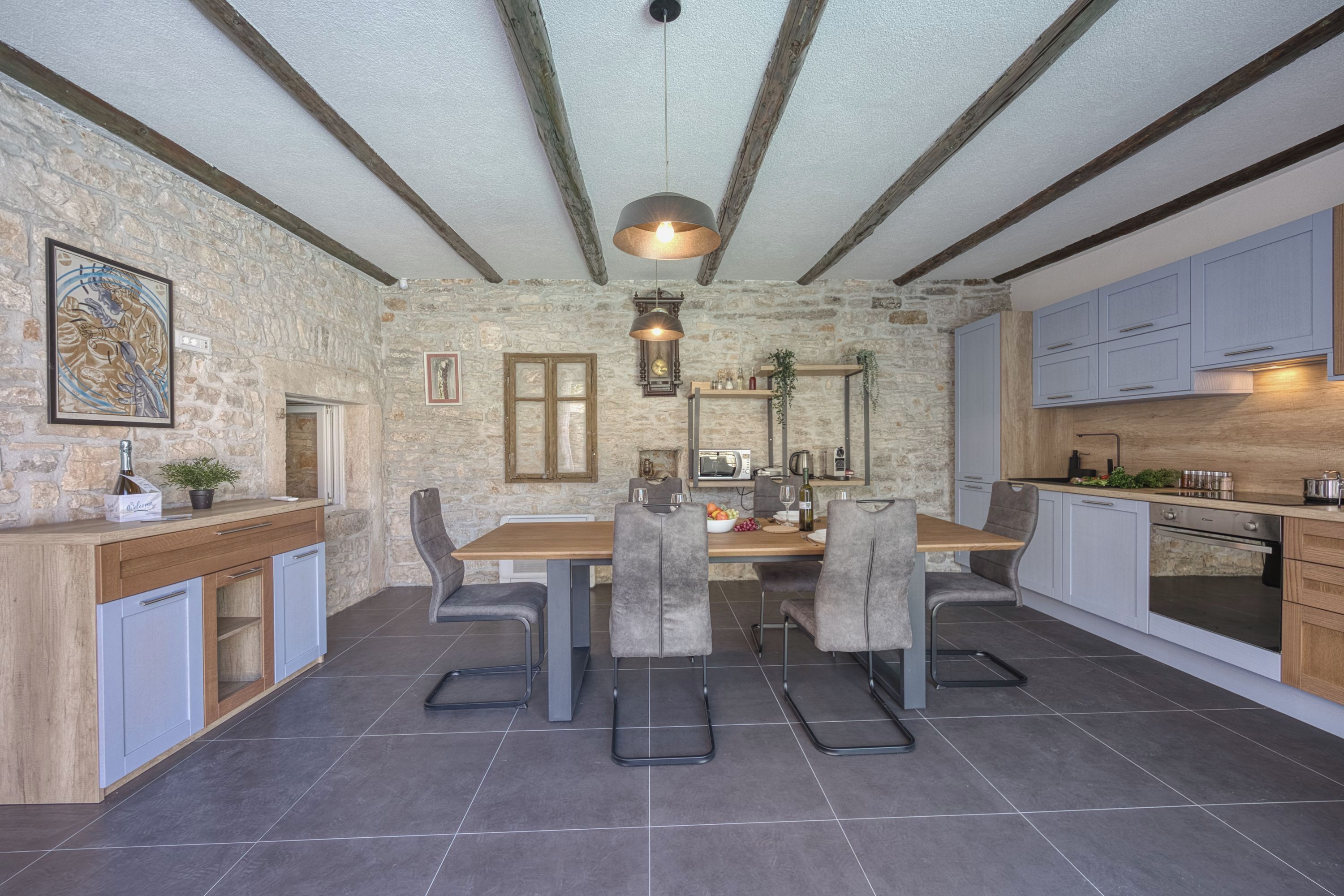 A modern kitchen with a stone wall, wooden beams, and grey chairs.