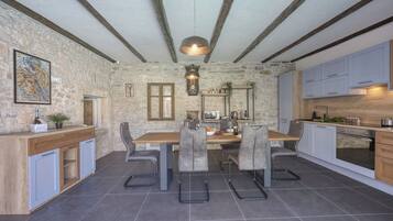 A modern kitchen with a stone wall, wooden beams, and grey chairs.
