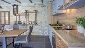 A modern kitchen with stone walls, wooden beams, and a dining area with a table and chairs.