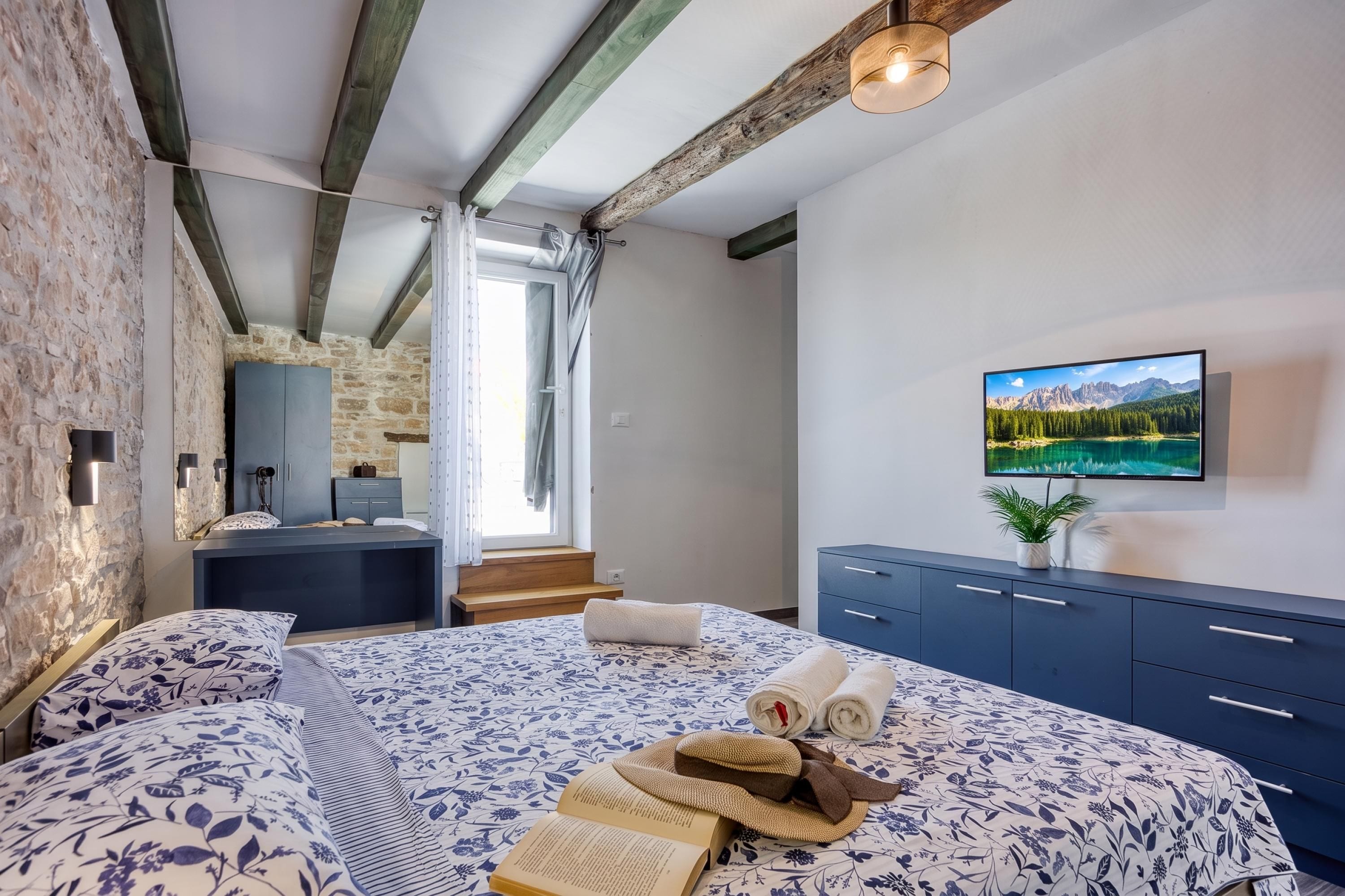 A bedroom with a bed, a TV, a dresser, and a window with curtains.