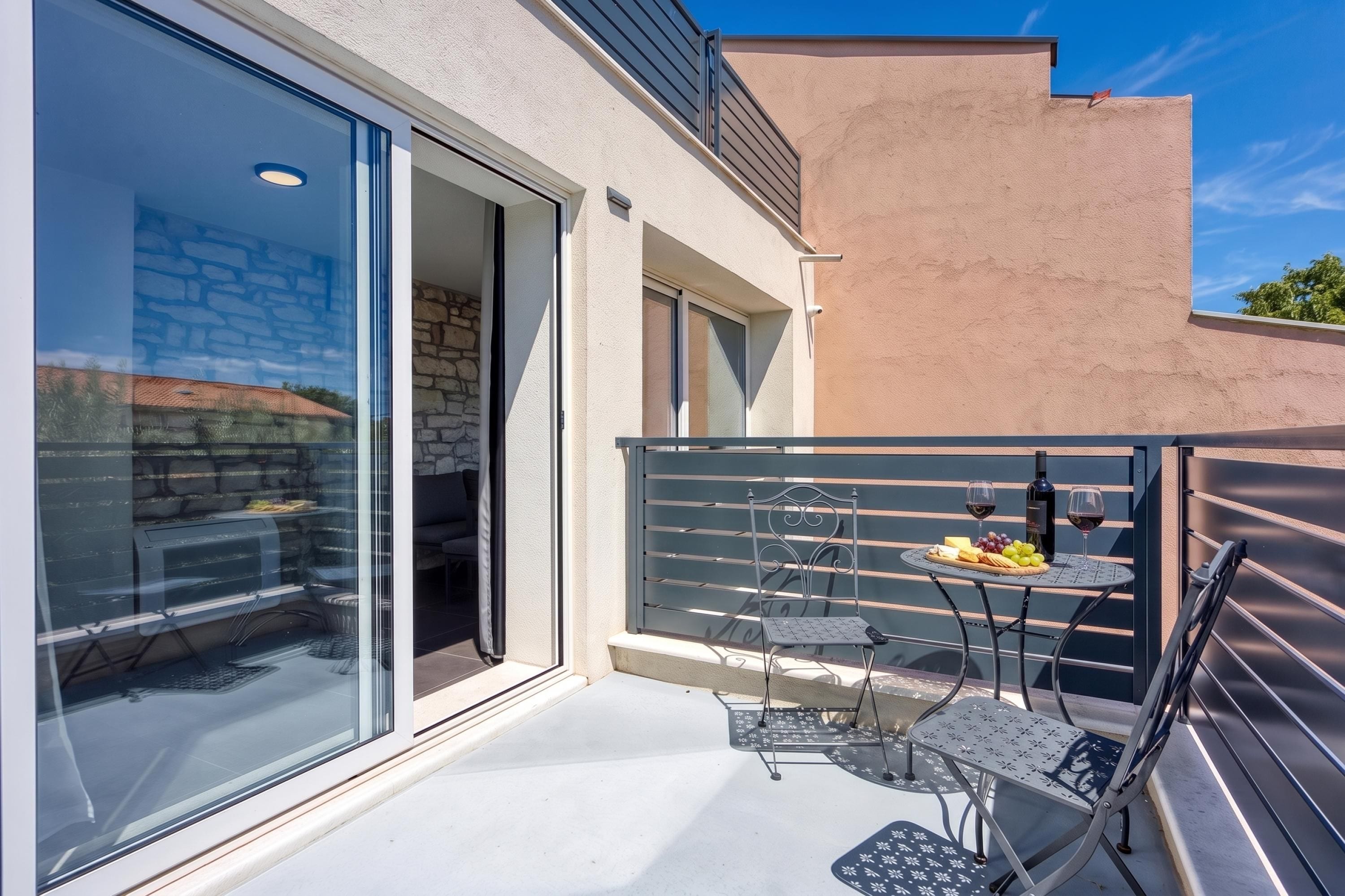 Un'area salotto esterna moderna con tavolo e sedie, una porta vetrata che dà su un patio e un tavolino con una bottiglia e dei bicchieri.