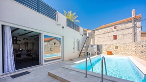 A modern building with a swimming pool, a dining area, and a staircase leading to a stone building.