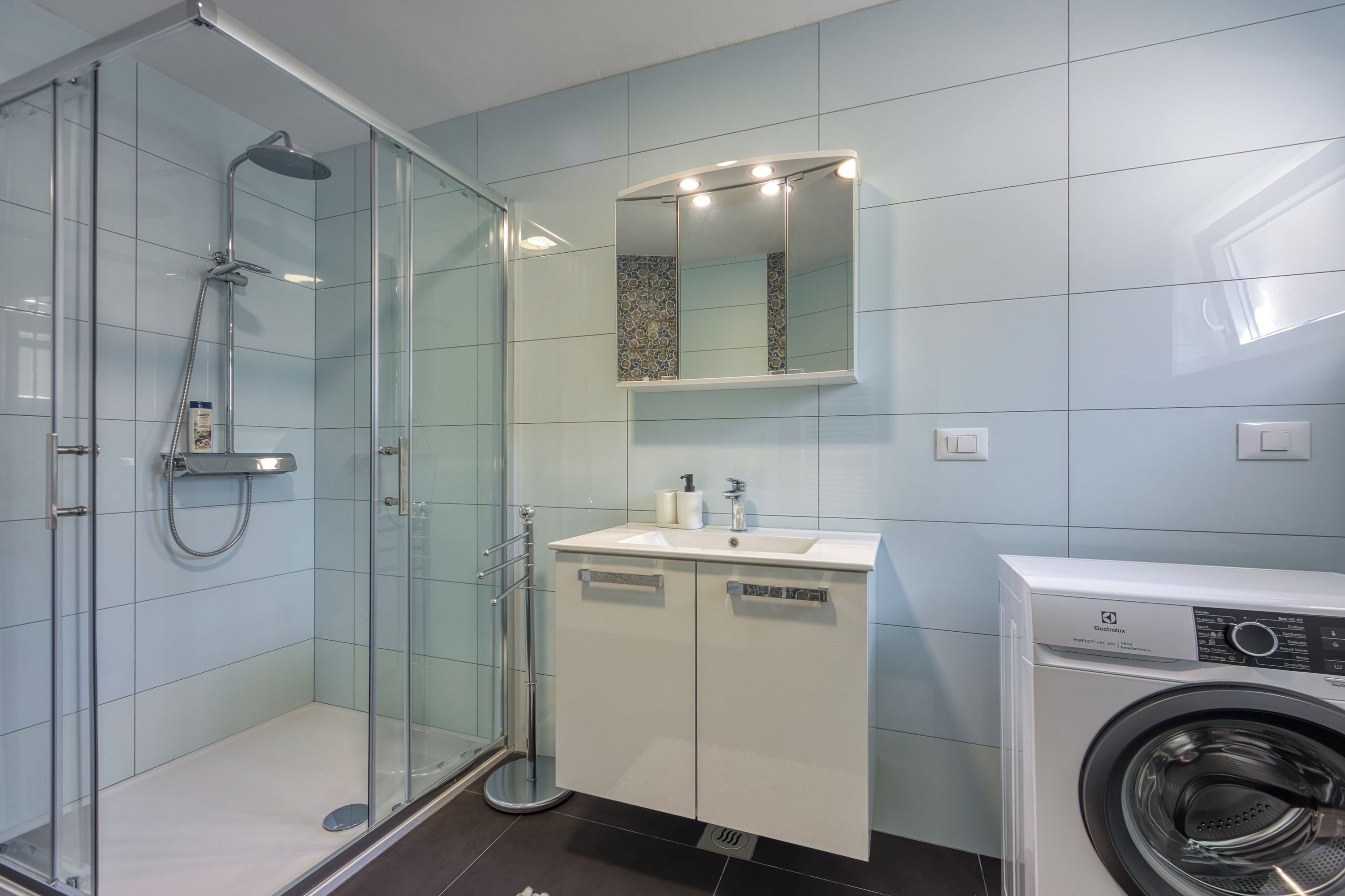 Une salle de bain moderne avec une douche à parois de verre, un lavabo avec un miroir et un lave-linge à chargement frontal.
