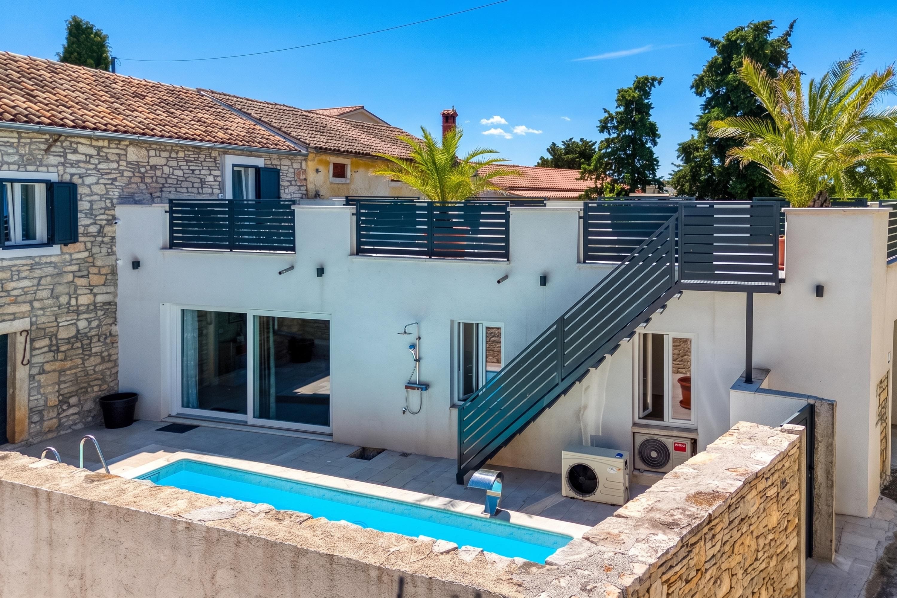 A modern villa with a swimming pool, a stone wall, and a staircase leading to a second floor.